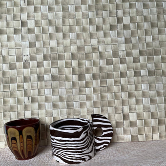A wallpaper with a geometric pattern featuring a combination of beige, white, and brown colors, displayed in a room setting with two cups on the foreground.
