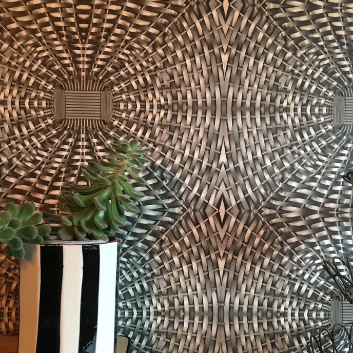 A section of wallpaper with a geometric diamond pattern in shades of silver and black, showcasing a woven metal design.