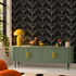 A styled interior scene showing a green ribbed sideboard with gold handles against a black wallpaper patterned with white birds. A yellow table lamp, a wooden duck figurine, a small yellow duck, colorful eggs, and a cup sit on top.