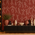 A styled interior scene with terracotta wallpaper featuring white line-drawn human figures, a black sideboard with decorative vases and sculptures, and a built-in shelving unit on the left with warm lighting.