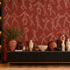 A styled interior scene with terracotta wallpaper featuring white line-drawn human figures, a black sideboard with decorative vases and sculptures, and a built-in shelving unit on the left with warm lighting.